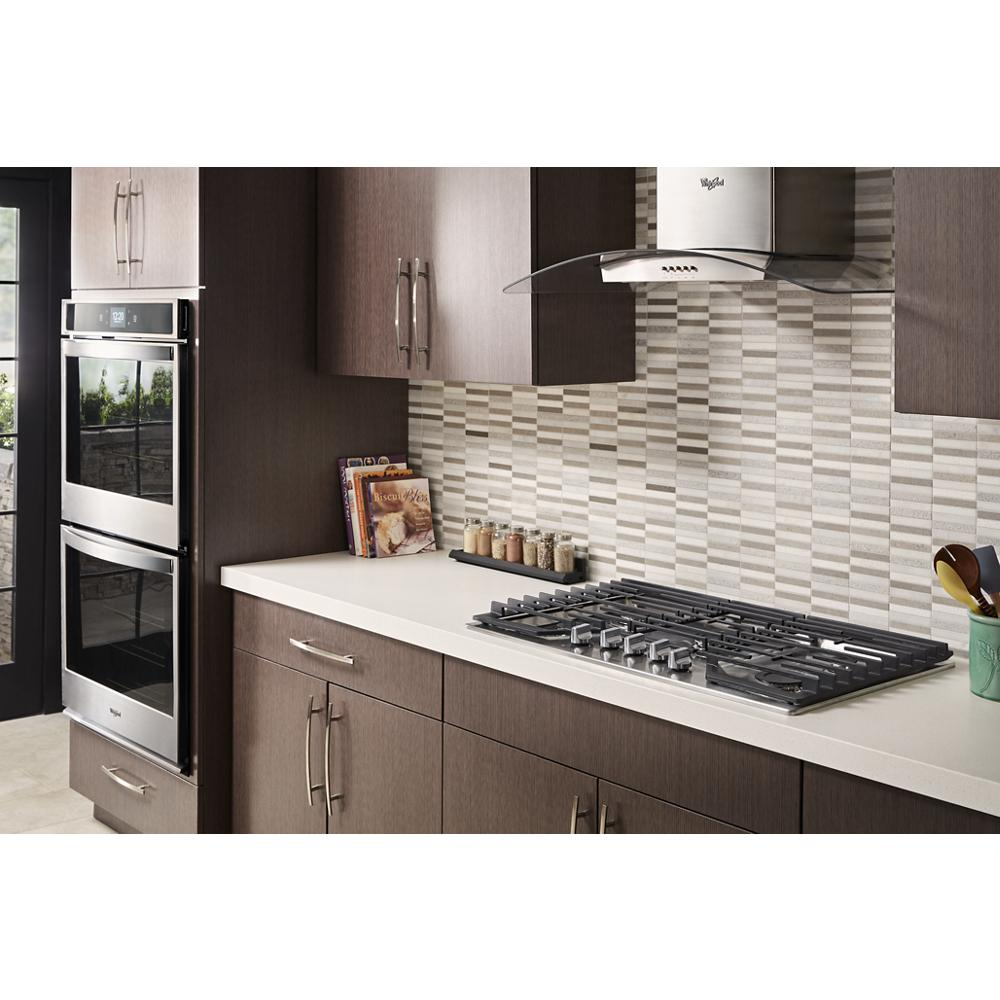 Modern kitchen with stainless steel glass wall mount range hood, gas cooktop, dark wood cabinets, and tiled backsplash