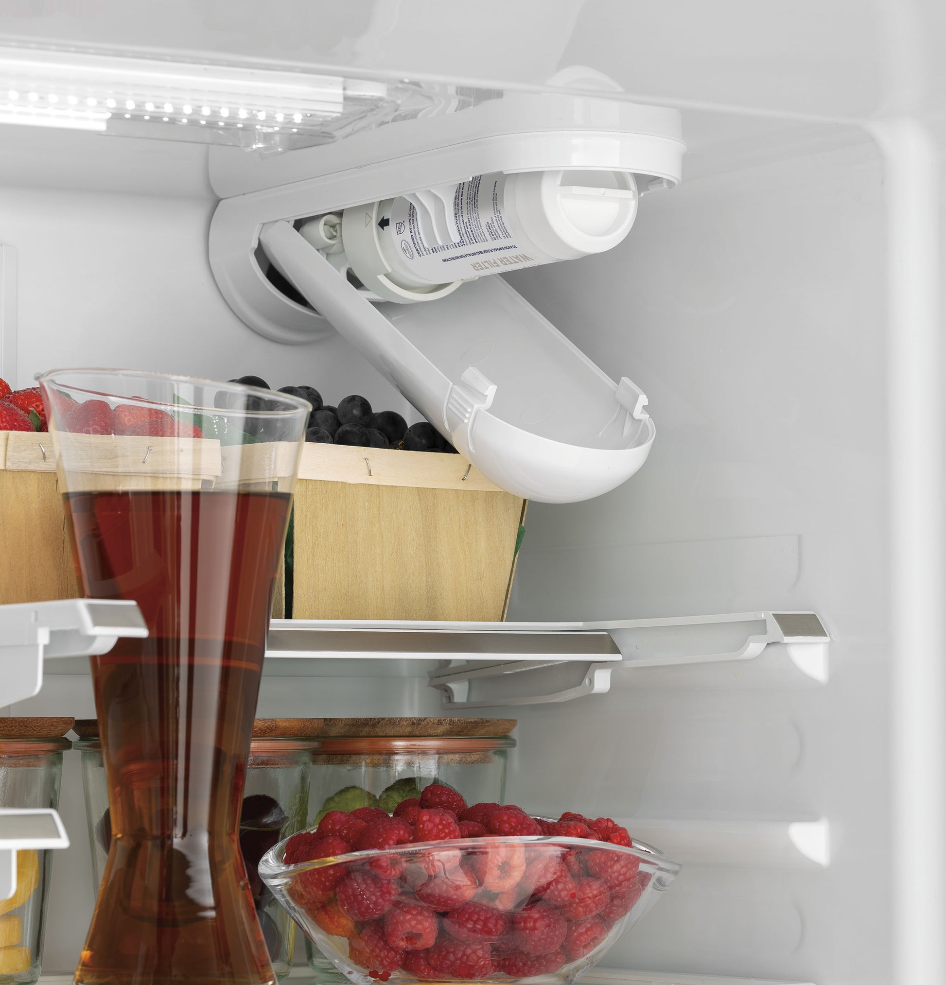 White French-door refrigerator interior shelf showing water filter and clear containers with berries and juice