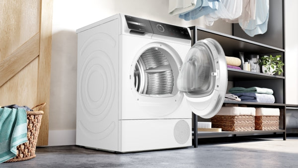 White Bosch heat pump dryer with open front door and circular drum, black control panel, in modern laundry space