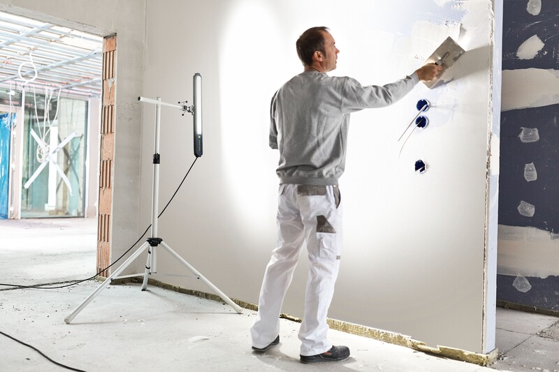 Aluminum tripod stand with locking pin supporting LED work light in unfinished room for tool and home improvement accessories