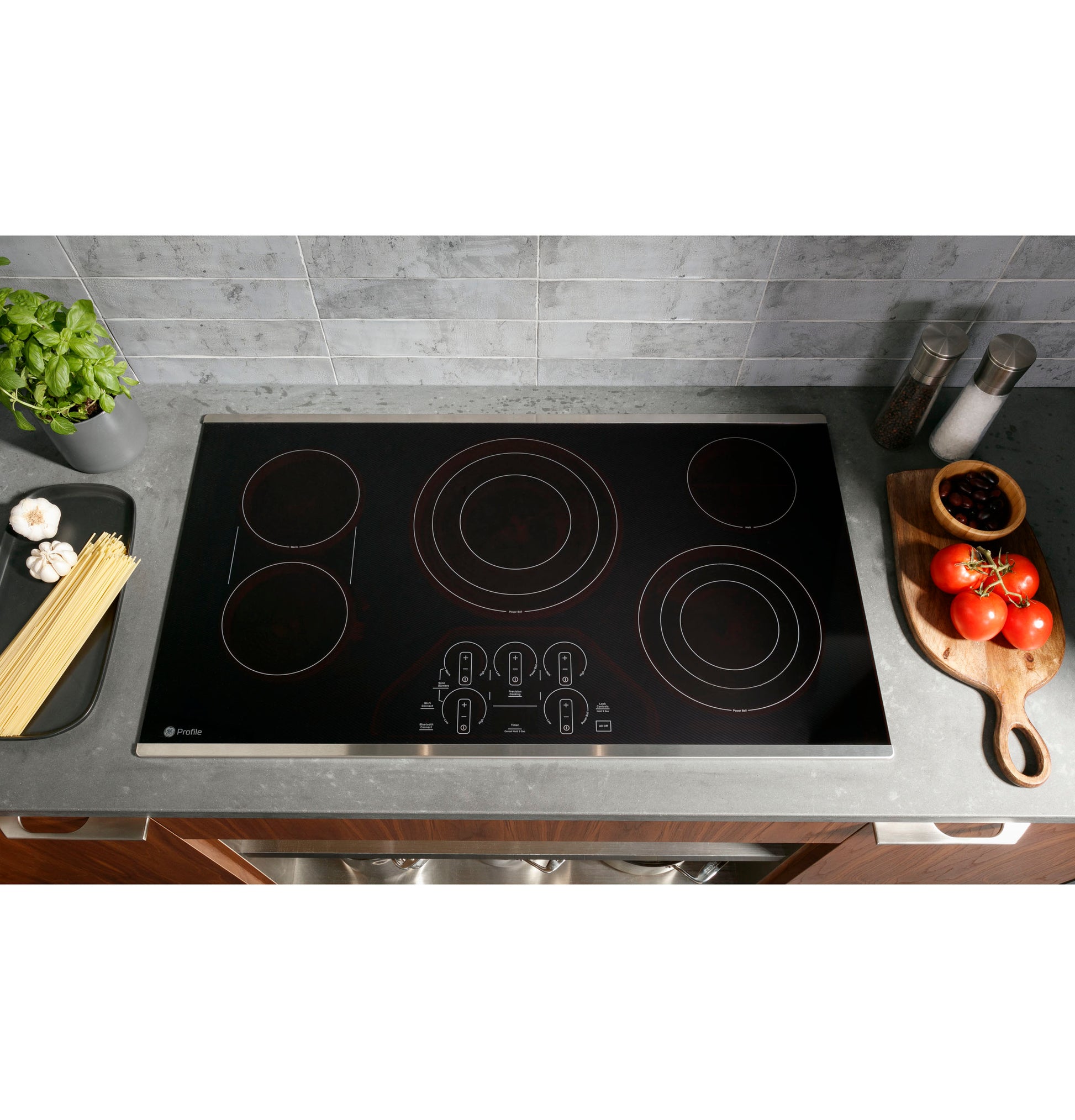 Black electric cooktop with touch controls installed in modern kitchen countertop with fresh ingredients nearby