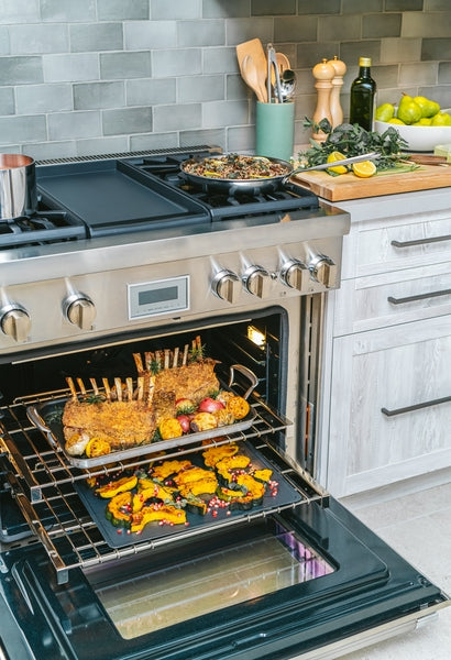 Stainless steel dual fuel range with open oven containing racks of roasted meat and vegetables in modern kitchen setting