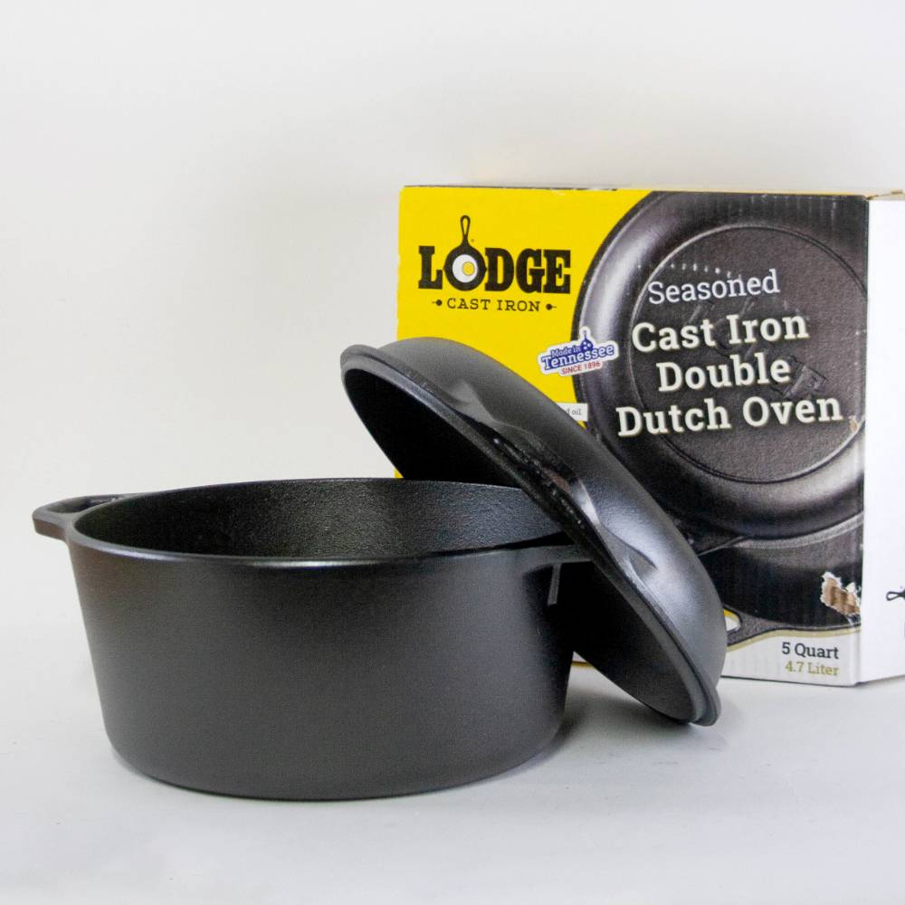 Black seasoned cast iron double Dutch oven with lid next to branded packaging in kitchenware collections under $100