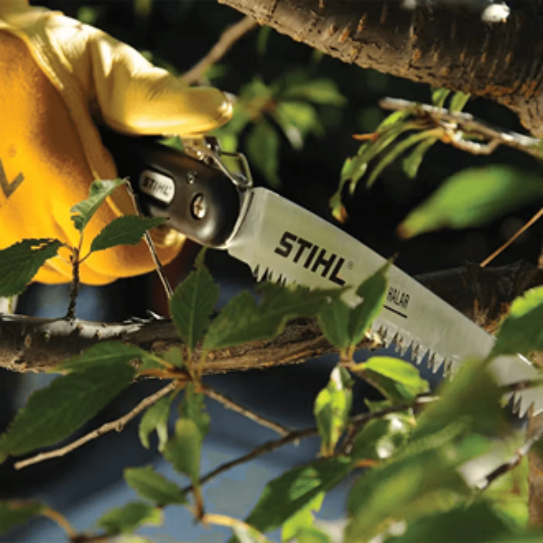 Gloved hand using a STIHL folding saw with hard chrome blade to cut a small tree branch in garden tools setting