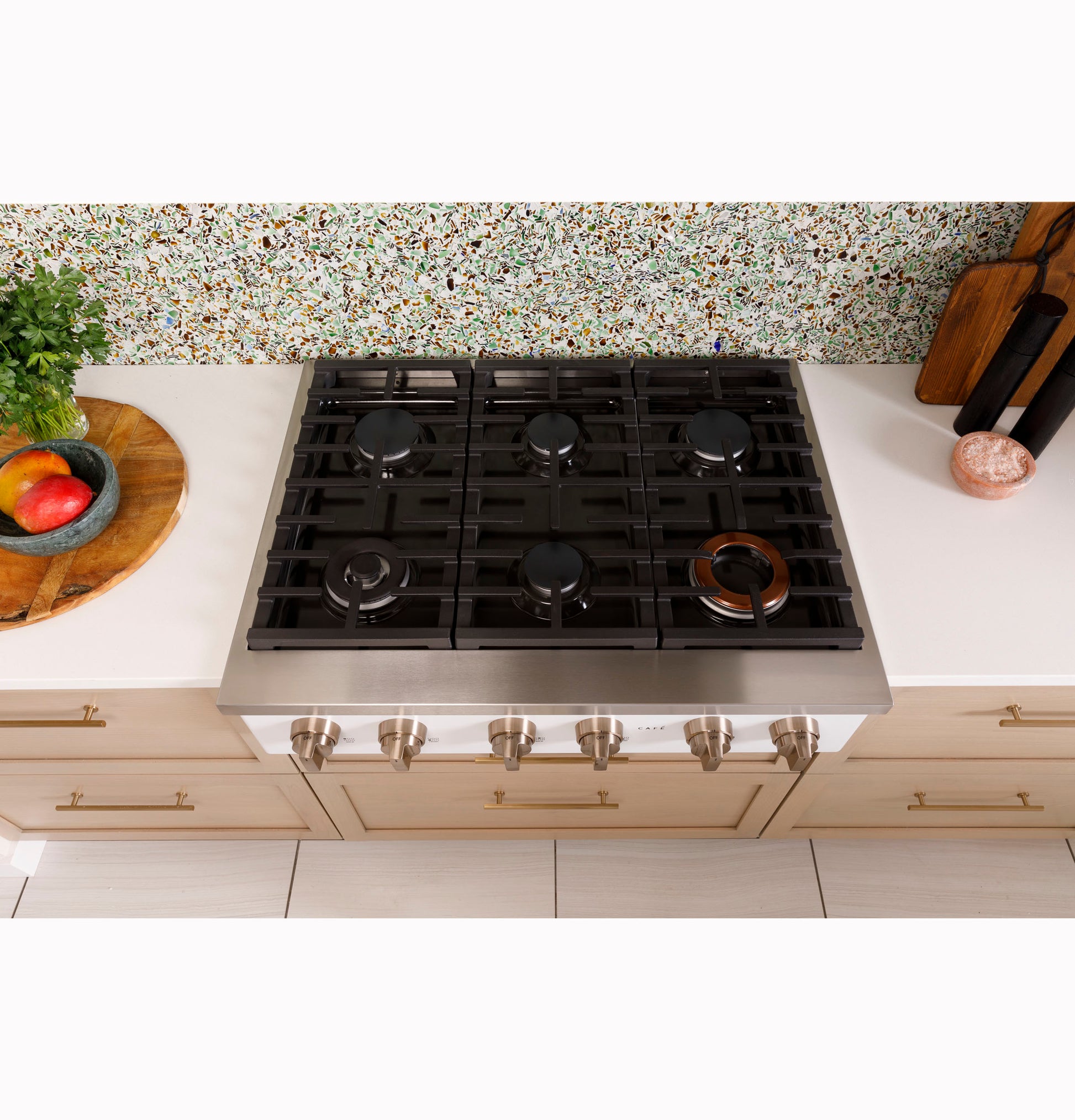 Top-down view of six-burner commercial-style gas rangetop installed in modern kitchen with light cabinetry and countertop decor
