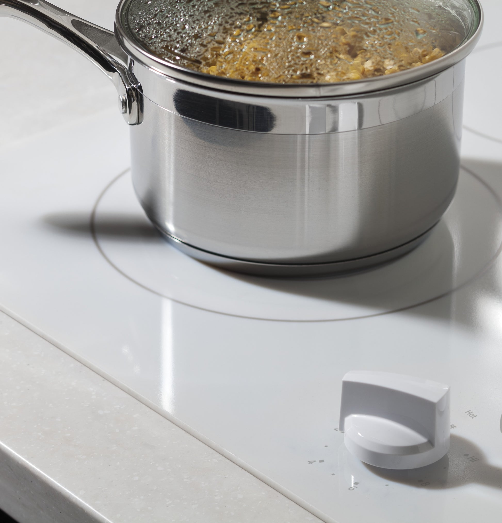 Stainless steel saucepan with lid simmering on white electric cooktop with knob control in kitchenware and appliances setting