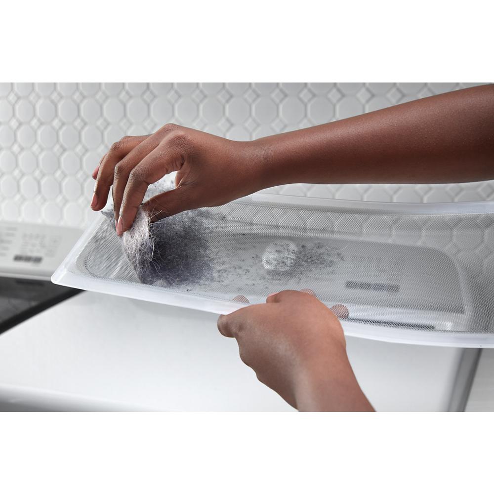 Hands removing lint and pet hair from a white dryer lint trap screen above a top load electric dryer in a laundry room