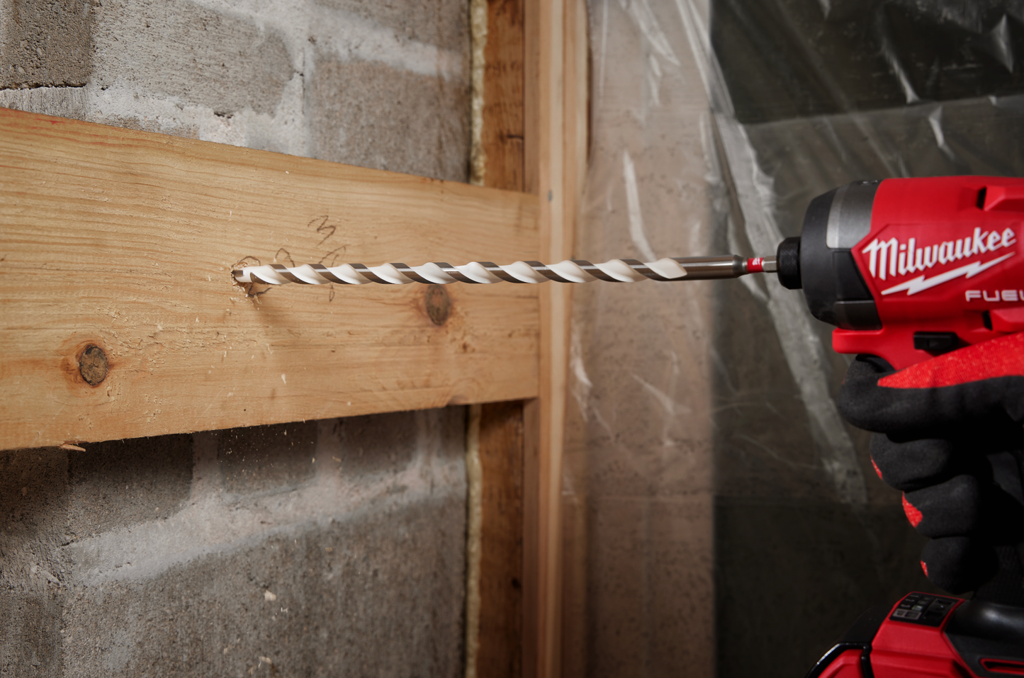 Red and black power drill with 1/8 inch carbide multi-material bit drilling into wooden plank in home improvement setting