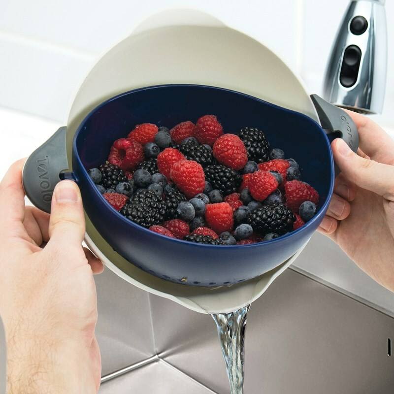 Deep indigo soak and strain colander draining mixed berries over kitchen sink in cooking utensil setting