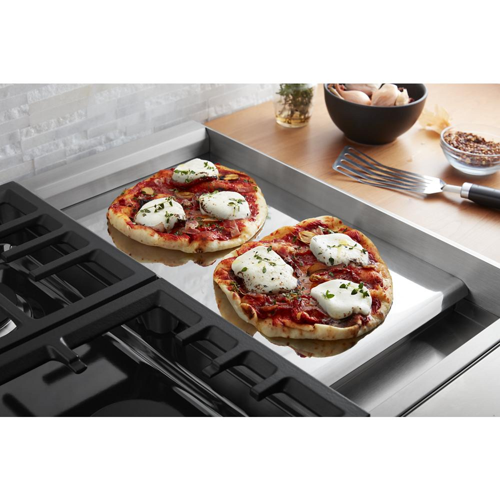 Two personal-size pizzas with melted cheese cooking on a chrome electric griddle beside a gas cooktop burner