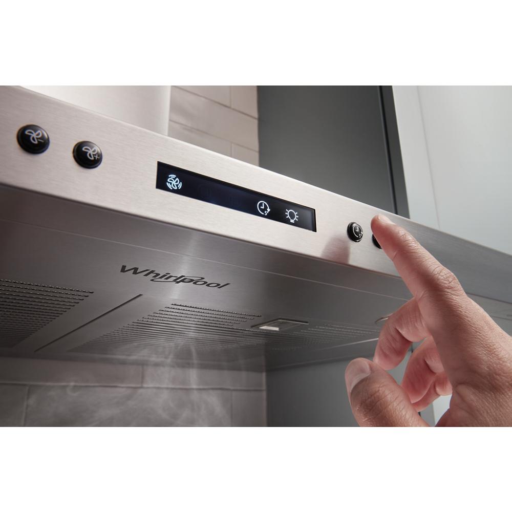 Hand adjusting control panel on stainless steel wall mount range hood with LED lights in kitchen appliances collection