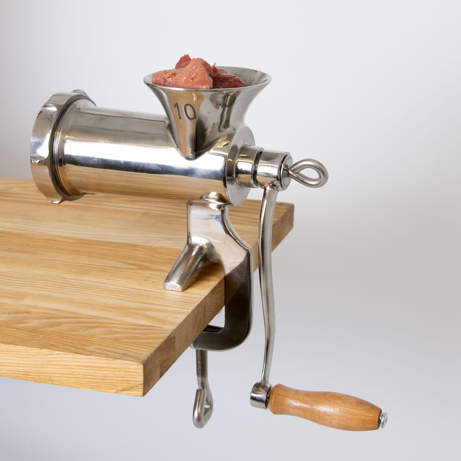 Stainless steel clamp-down meat grinder with wooden handle attached to wood table in kitchen appliances under $100