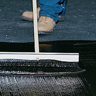 Close-up of a person applying blacktop filler with a squeegee on an asphalt surface for home improvement projects