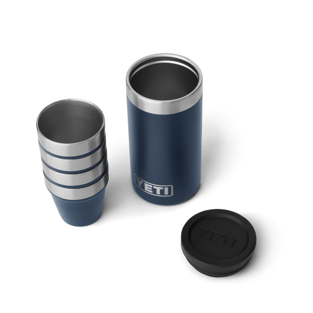 Set of four navy blue shot glasses stacked next to matching insulated carrying case with YETI logo in drinkware collection