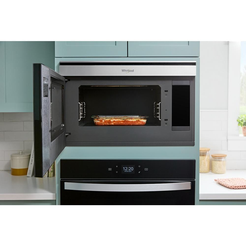 Built-in smart microwave oven with stainless steel trim and open door showing casserole inside in modern kitchen setup