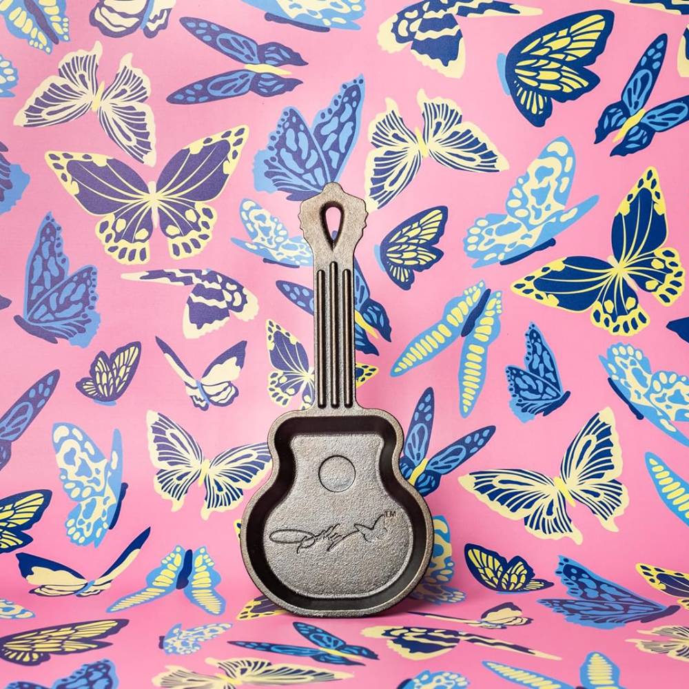 Miniature cast iron skillet shaped like a guitar with engraved signature on colorful butterfly patterned background