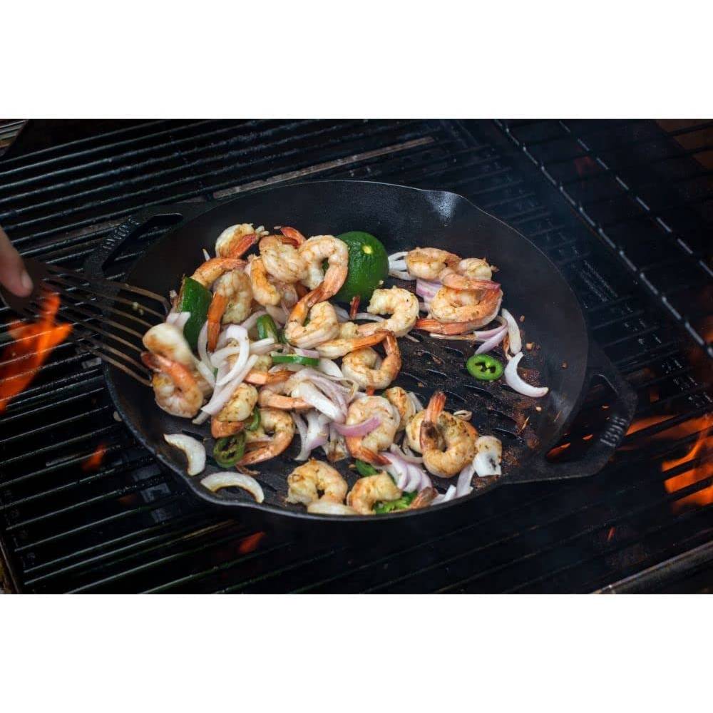 Seasoned cast iron grilling basket with dual handles cooking shrimp, onions, and jalapeños over an open flame in kitchenware collection