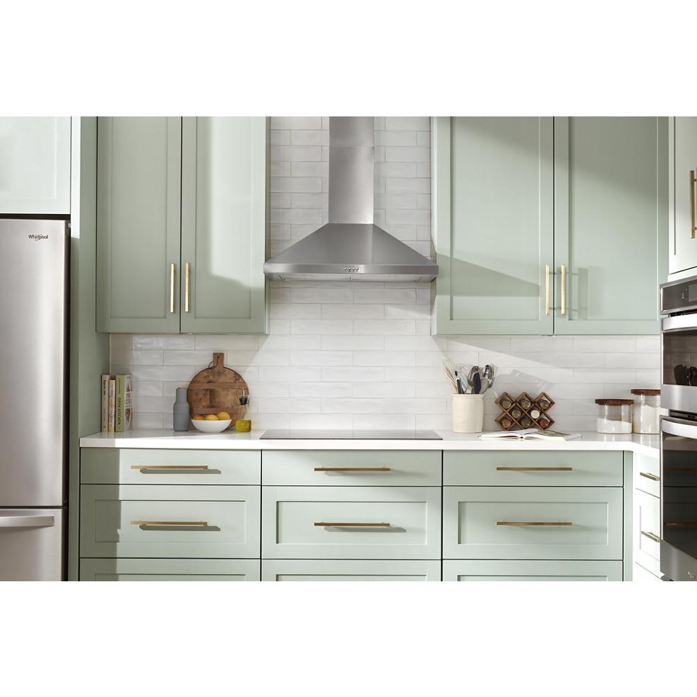 Modern kitchen with stainless steel chimney hood over cooktop, light green cabinetry, and white subway tile backsplash