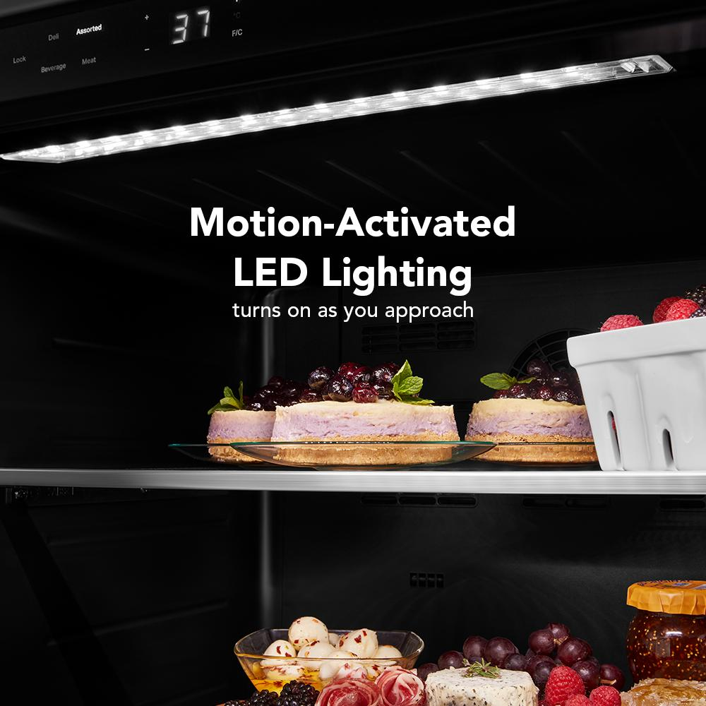Interior view of refrigerator interior spotlighted by motion-activated LED light with desserts and fruit on glass shelves
