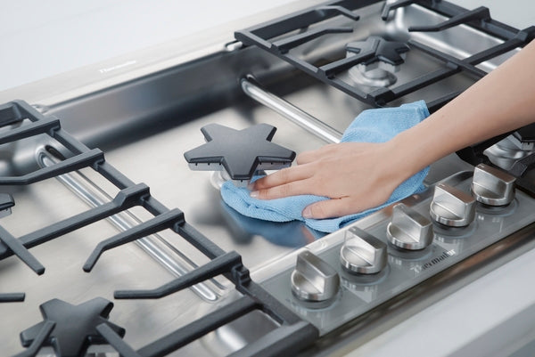 Hand wiping stainless steel 36-inch gas cooktop surface with blue cloth in modern kitchen setting