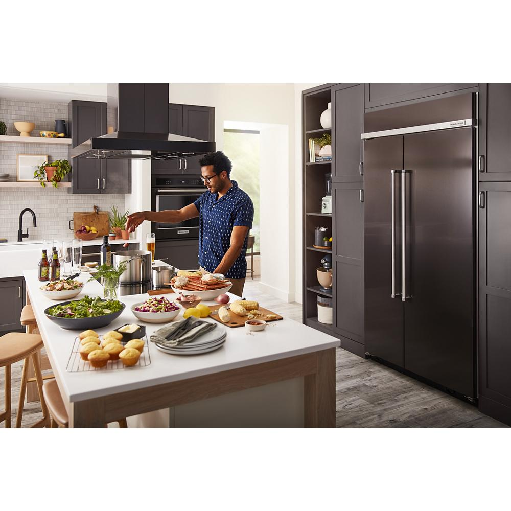 Man cooking in modern kitchen with island set for meal and built-in appliances in dark cabinetry