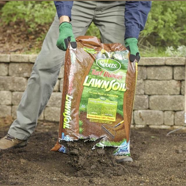 Person wearing gloves pouring soil from a bag onto garden bed for lawn improvement tasks