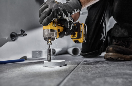 Yellow and black impact tool cutting a clean hole in a white PVC pipe during home improvement work
