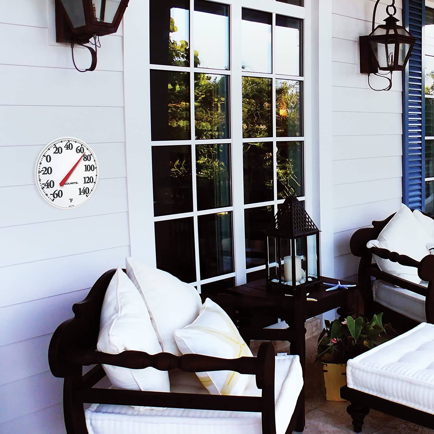 White outdoor wall thermometer with black numbers and red needle mounted on white siding near patio seating area