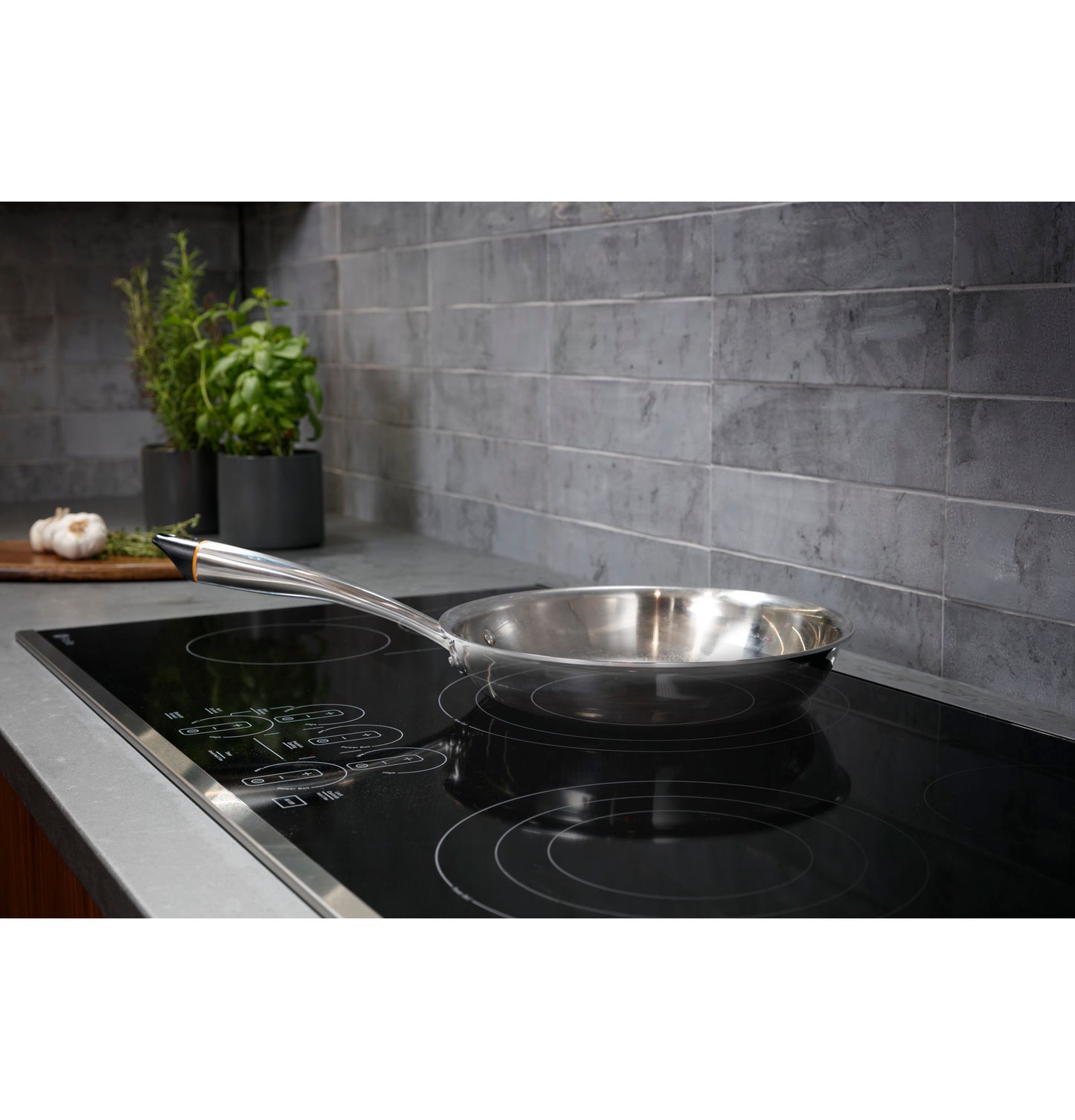 Stainless steel pan on black electric cooktop with touch controls set against gray tile backsplash in kitchen