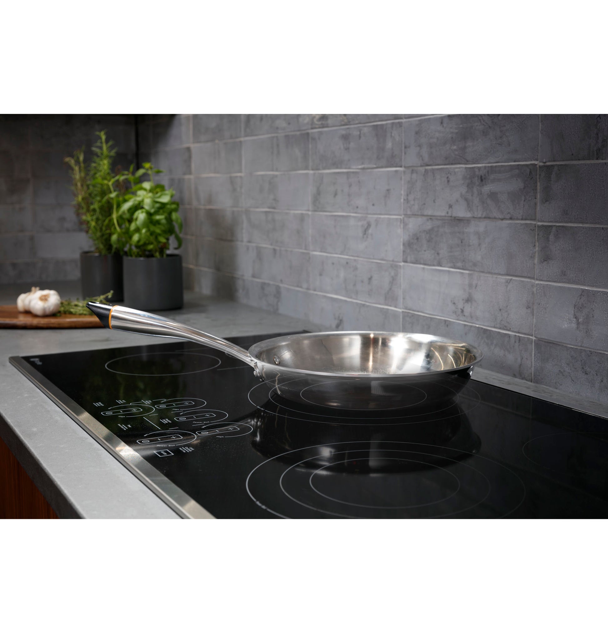 Stainless steel pan on black electric cooktop with touch controls set against gray tile backsplash in kitchen