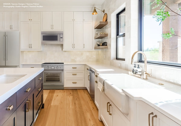 Bright modern kitchen with stainless steel appliances, white cabinetry, wood flooring, and large farmhouse sink in home improvement setting