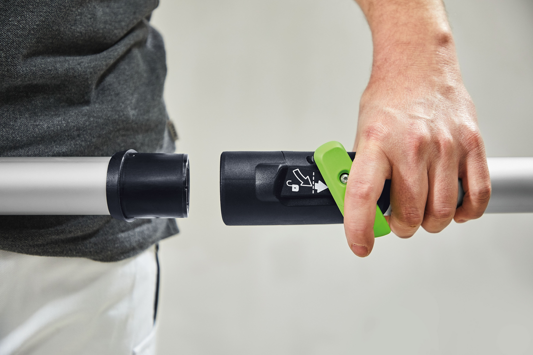 Person connecting gray and black extendable pole with green lever for tools and home improvement tasks