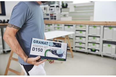 Person holding Festool Granat D150 starter set box in a workshop with storage cabinets for home improvement tasks