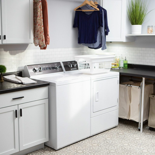 White electric dryer beside matching washer in bright laundry room with hanging clothes and modern cabinetry