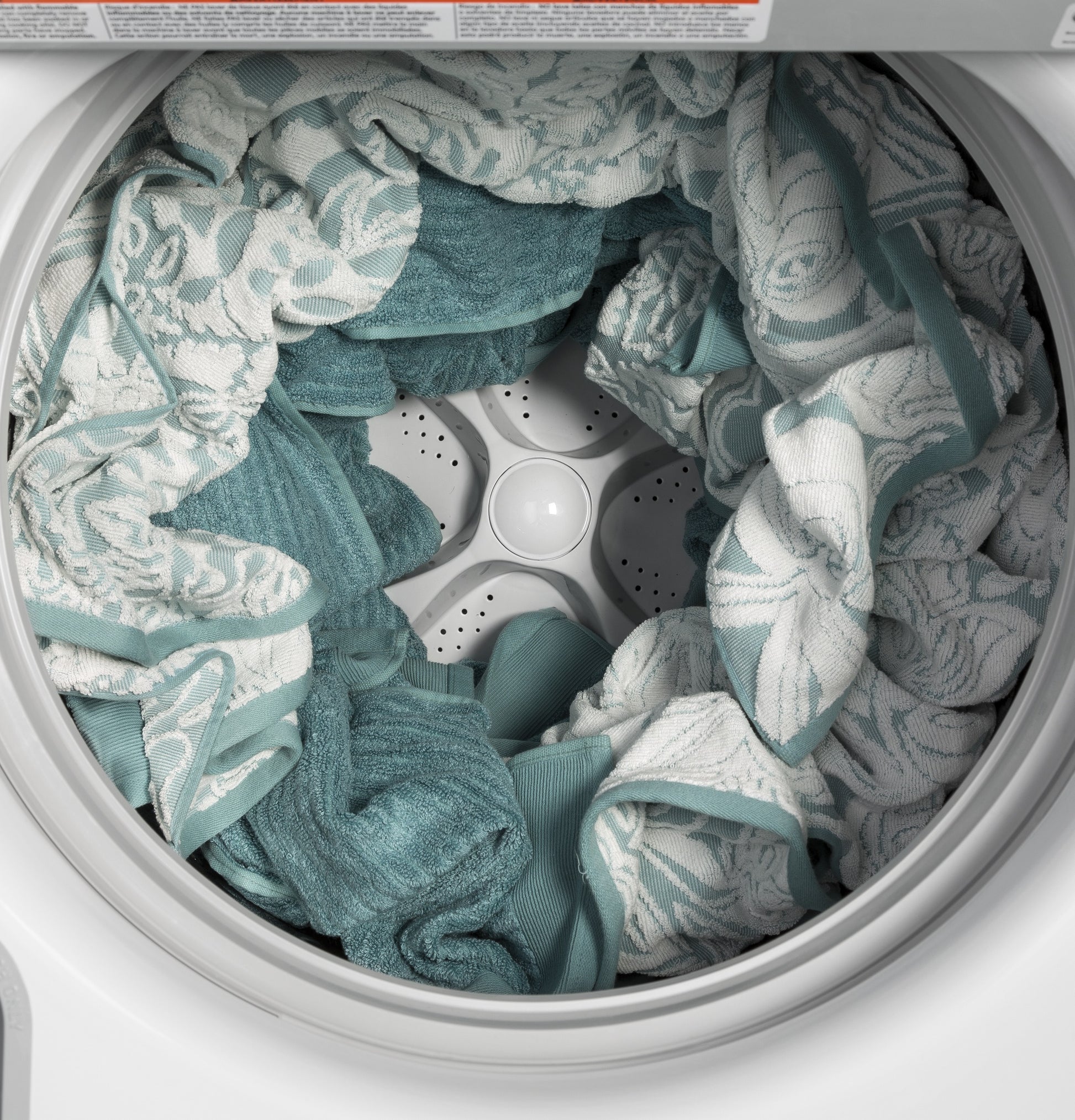 Top load washer filled with teal and white patterned towels in stainless steel basket from washers collection
