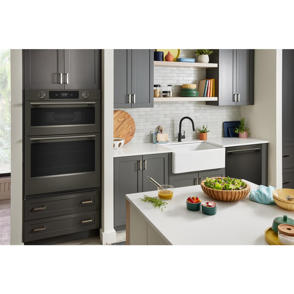 Modern kitchen with black ore combo wall oven, dark gray cabinets, white farmhouse sink, and fresh salad on island counter
