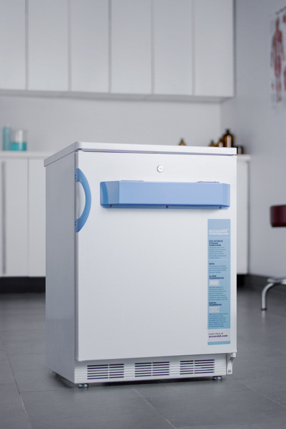 Compact white medical refrigerator with blue handle and label in modern clinical room setting
