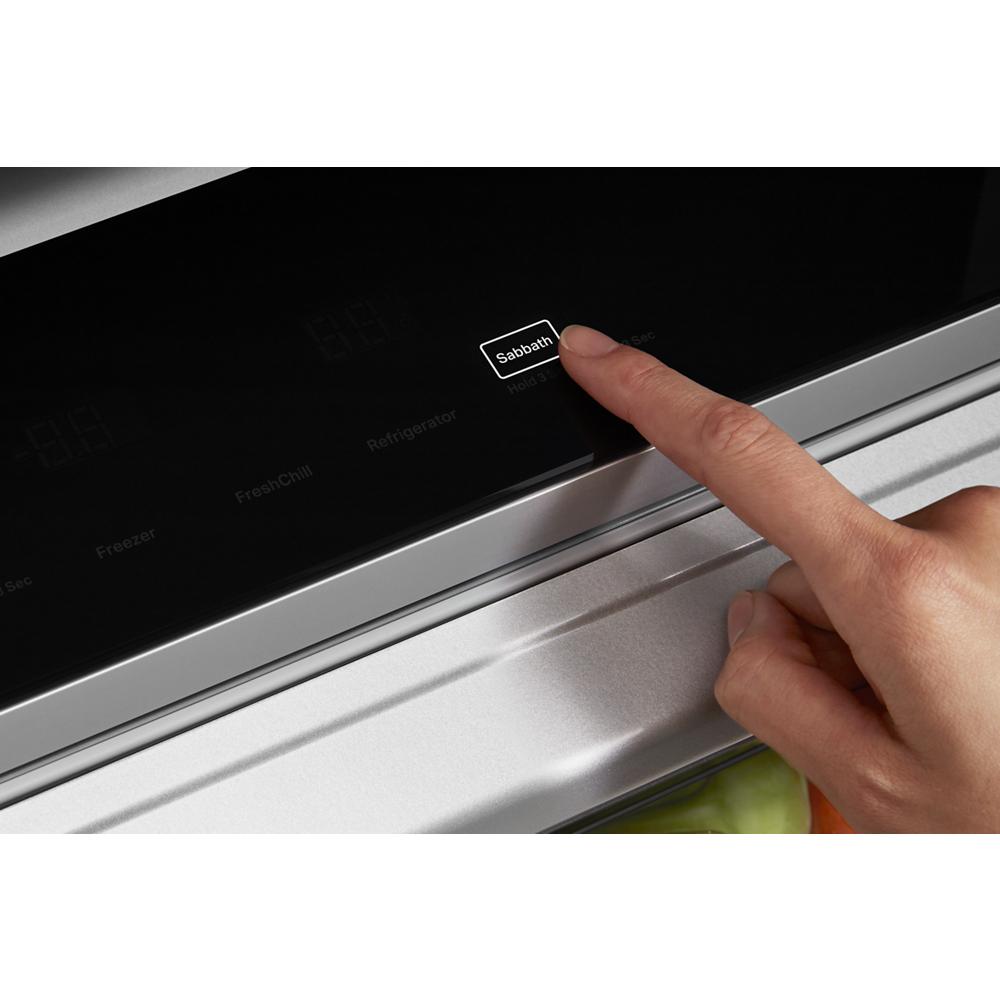 Close-up of finger pressing Sabbath mode button on black digital control panel of built-in side-by-side refrigerator