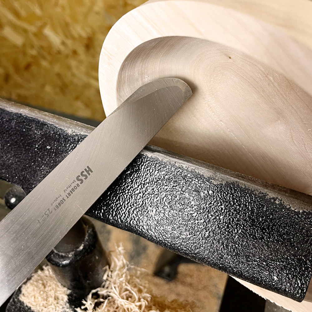 Close-up of a bowl turning tool shaping the inside curve of a spinning wooden bowl for woodworking tasks