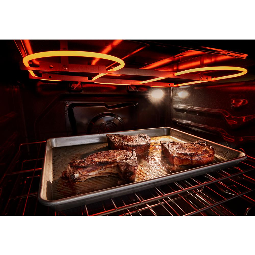 Close-up of three seared pork chops cooking on baking sheet inside glowing electric oven from kitchen appliances collection
