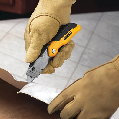 Hand wearing gloves holding DEWALT retractable folding utility knife cutting a material in home improvement tools collection