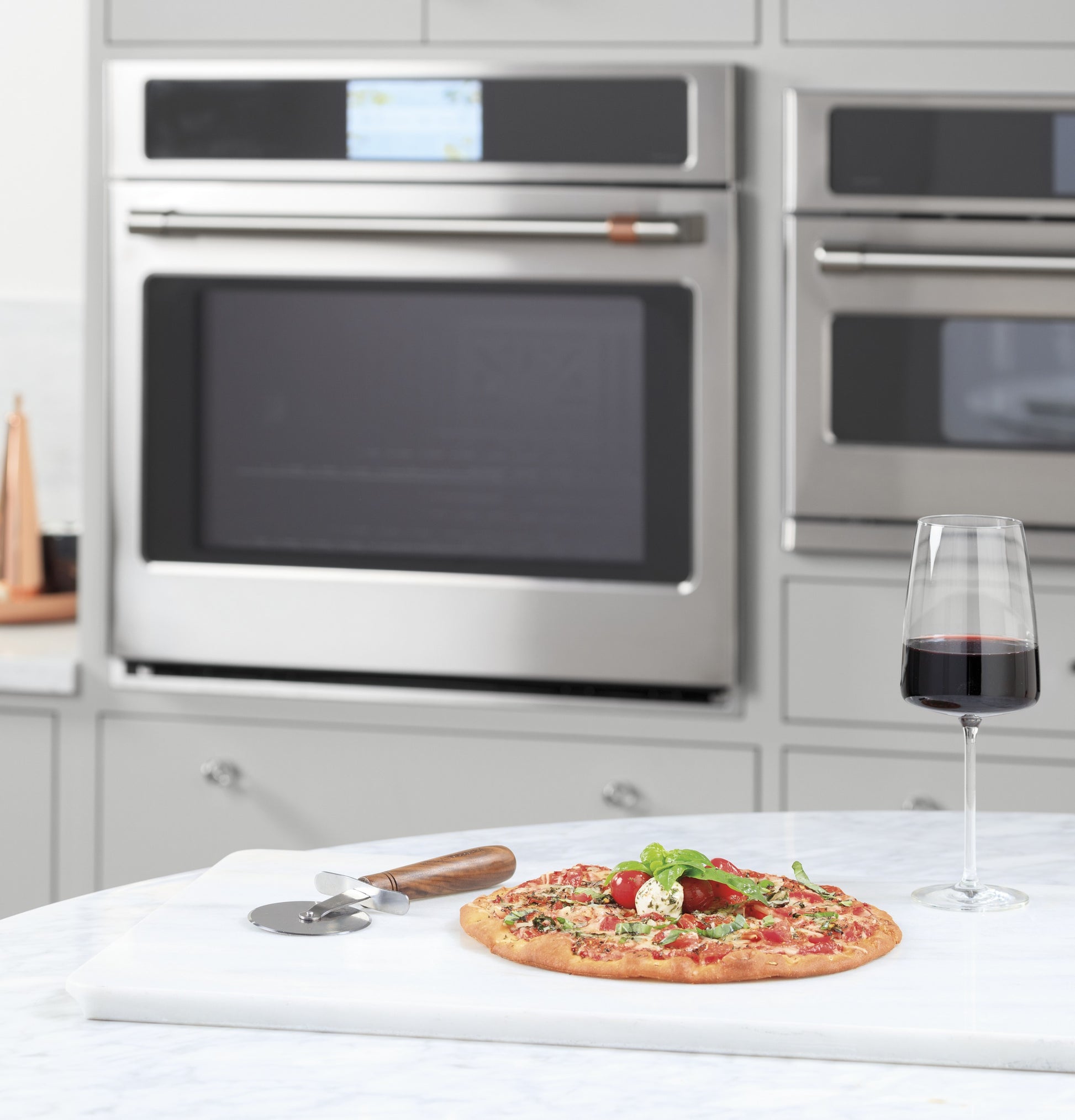 Margherita pizza with fresh basil on marble countertop next to glass of red wine in modern kitchen with double wall oven