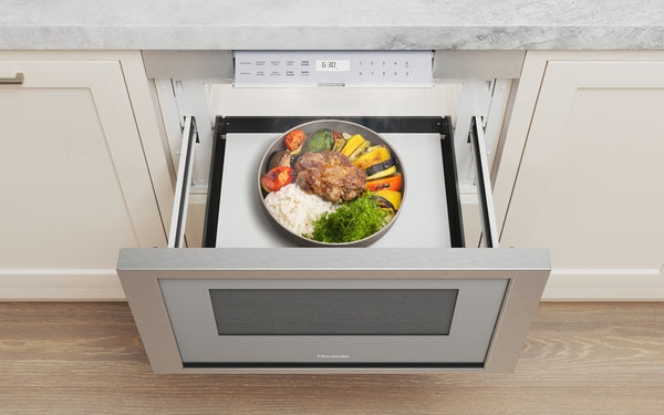 Built-in stainless steel microwave drawer open with a plated meal inside in modern kitchen setting