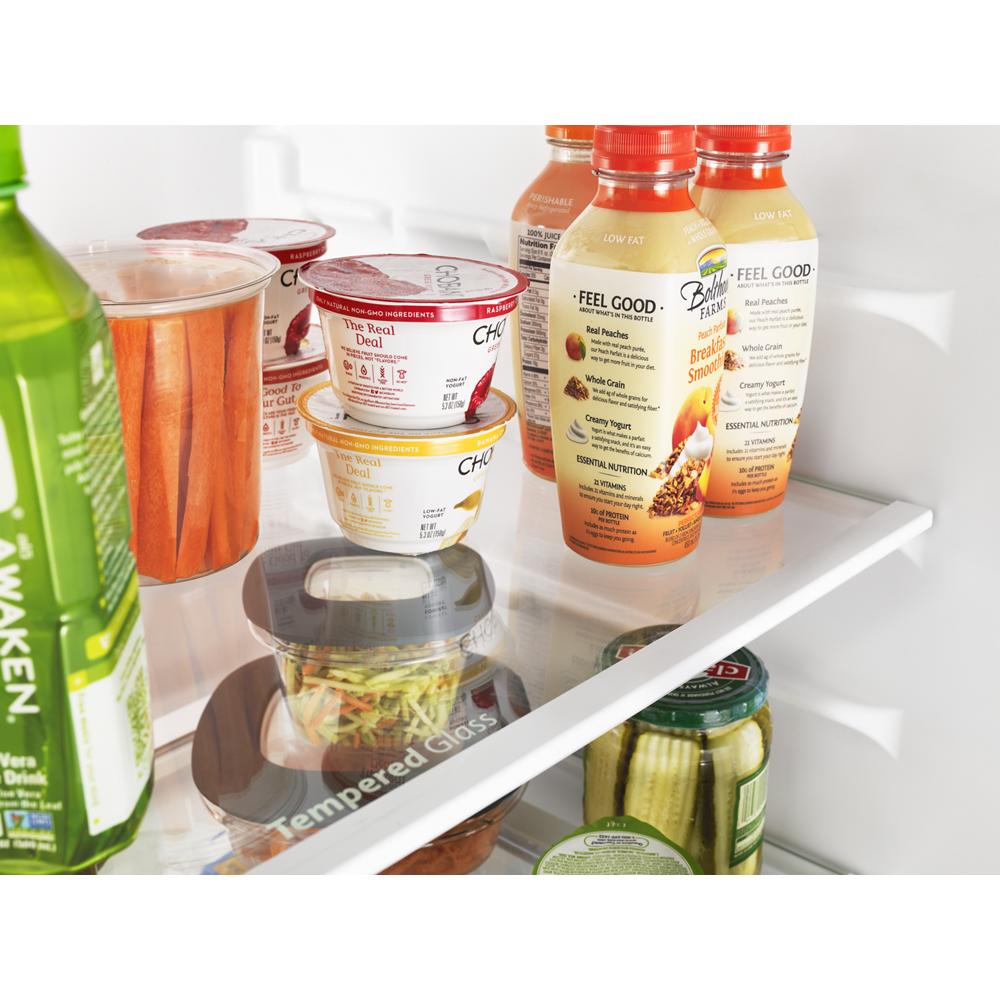Close-up of refrigerator shelf with drinks, packaged snacks, carrot sticks, and pickles in kitchen appliance setting