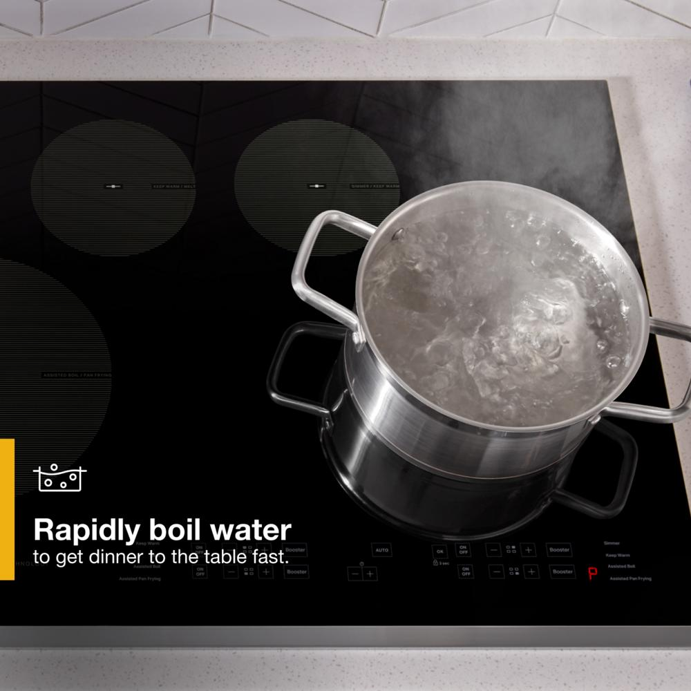 Stainless steel pot boiling water on sleek black glass induction cooktop in modern kitchen setting