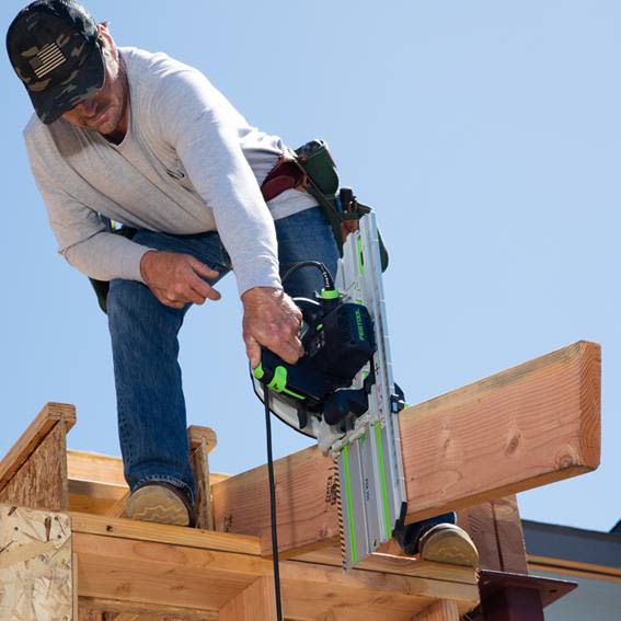 Carpenter using a Festool cordless saw with guide rail to make precise cuts on wooden beams outdoors