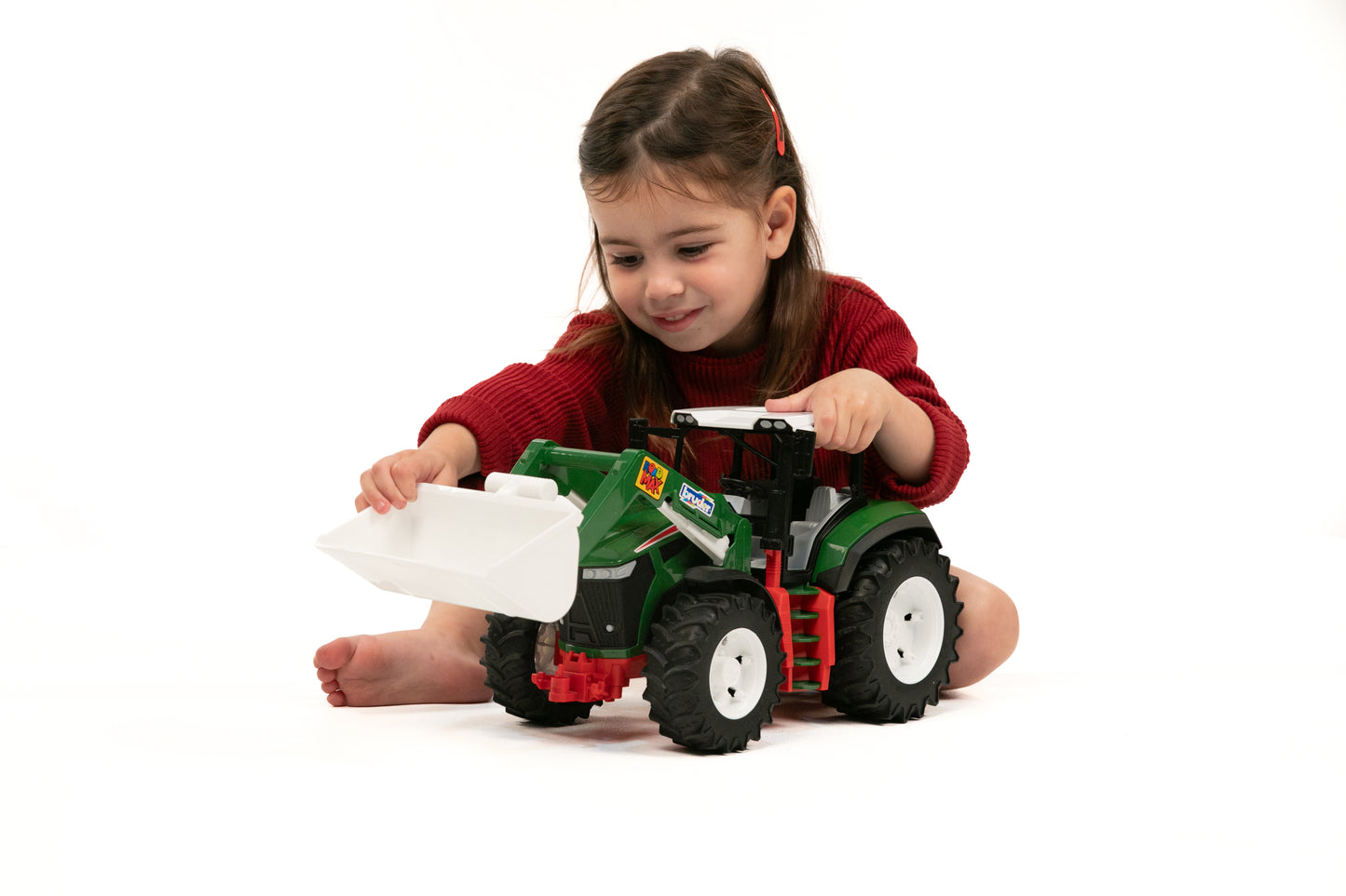 Child playing with a green and red toy tractor featuring a white frontloader bucket for imaginative play