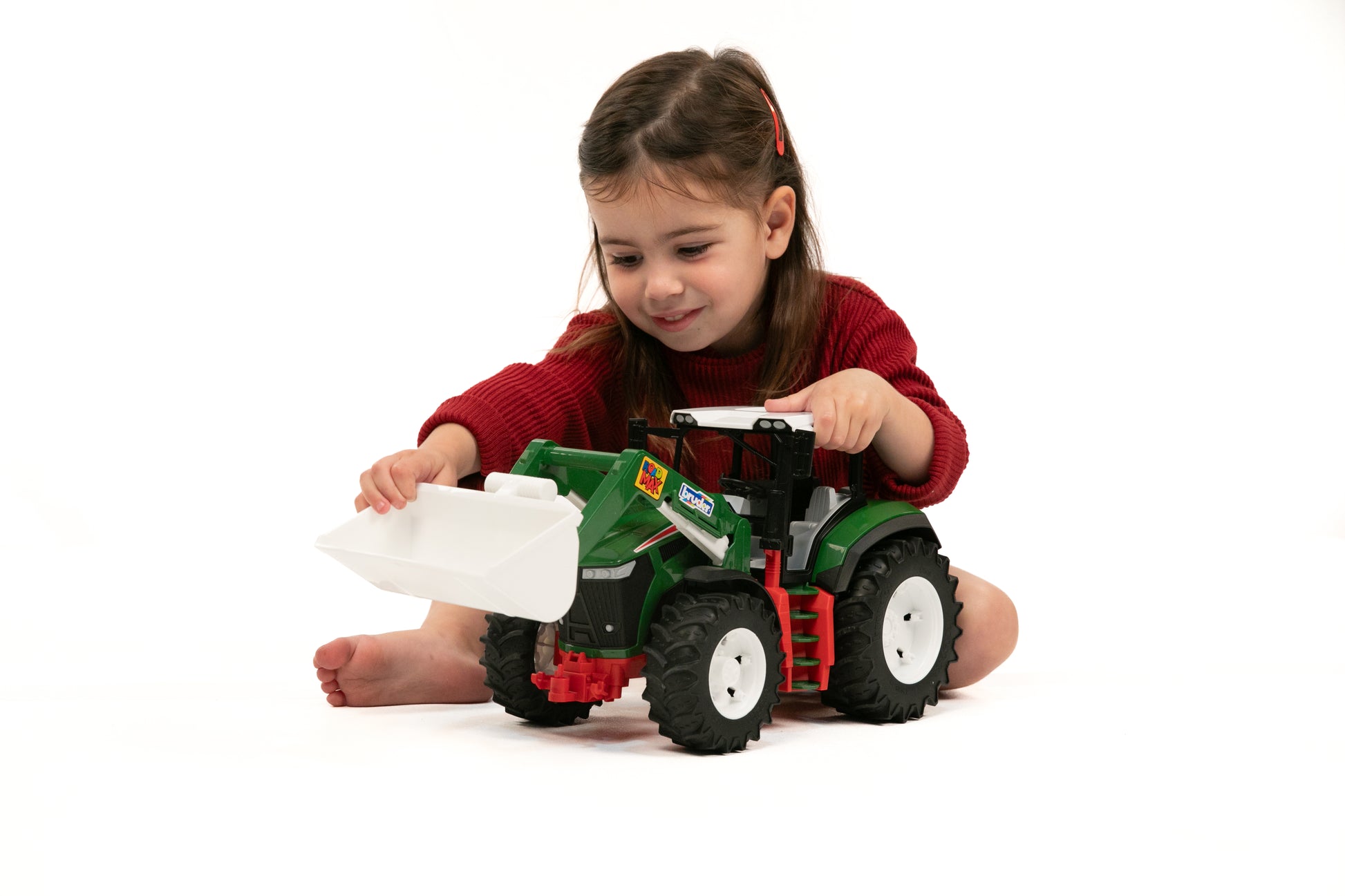 Child playing with a green and red toy tractor featuring a white frontloader bucket for imaginative play