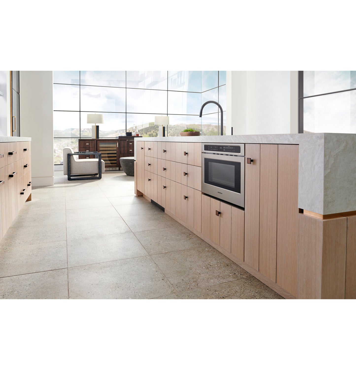 Built-in stainless steel microwave drawer integrated into light wood cabinetry in modern kitchen with large windows and tile floor