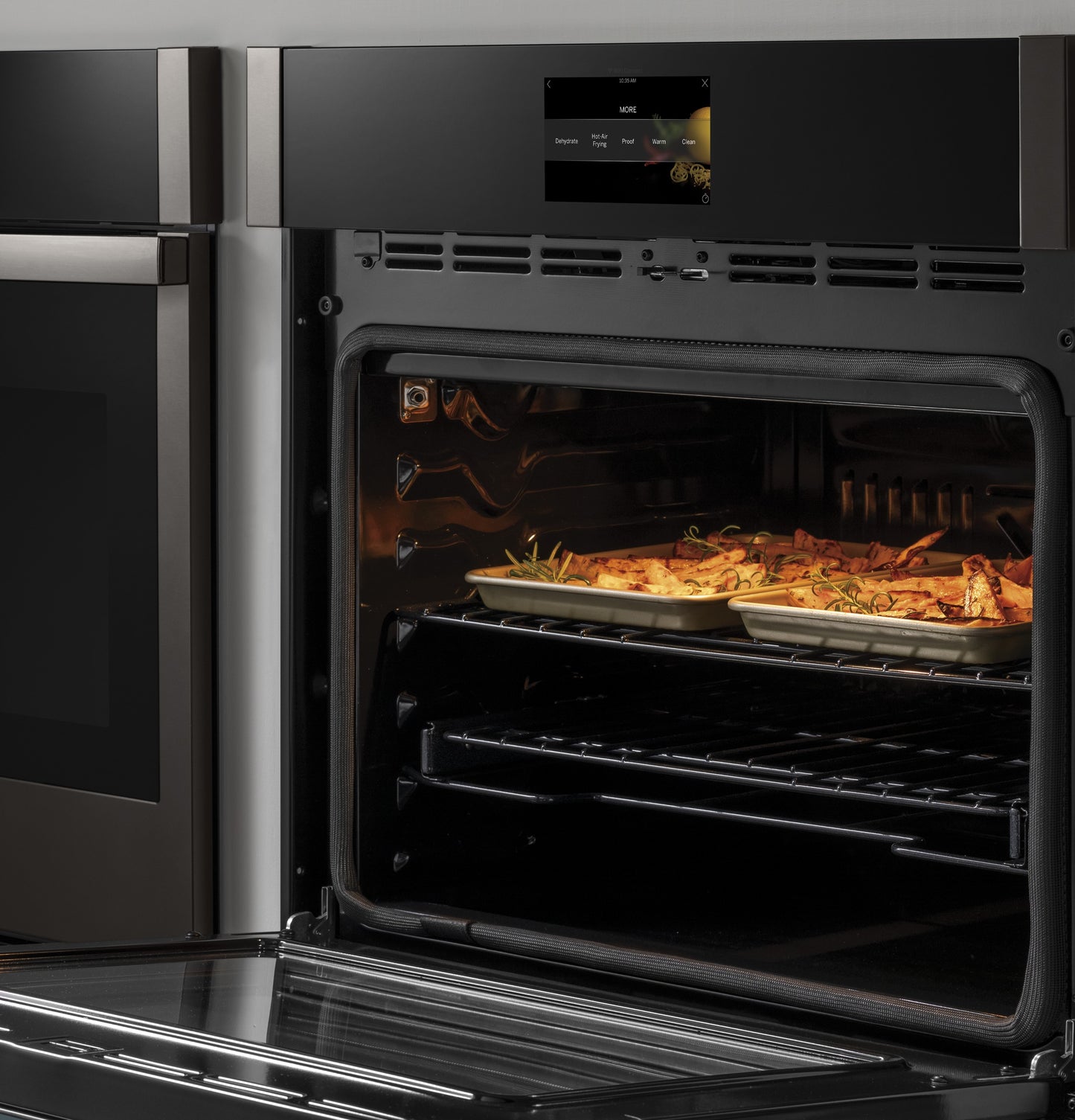 Open stainless steel built-in wall oven with trays of roasted food and digital control panel in kitchen appliances collection